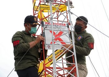 Dua personel Satpol PP menempelkan tanda silang merah pada menara telekomunikasi yang disegel karena tidak memiliki Izin Mendirikan Bangunan (IMB).
