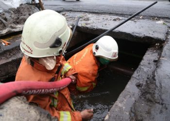 Dua personel Dinas Pemadam Kebakaran dan Penyelamatan menyemprot saluran agar tidak ada halangan air untuk mengalir.