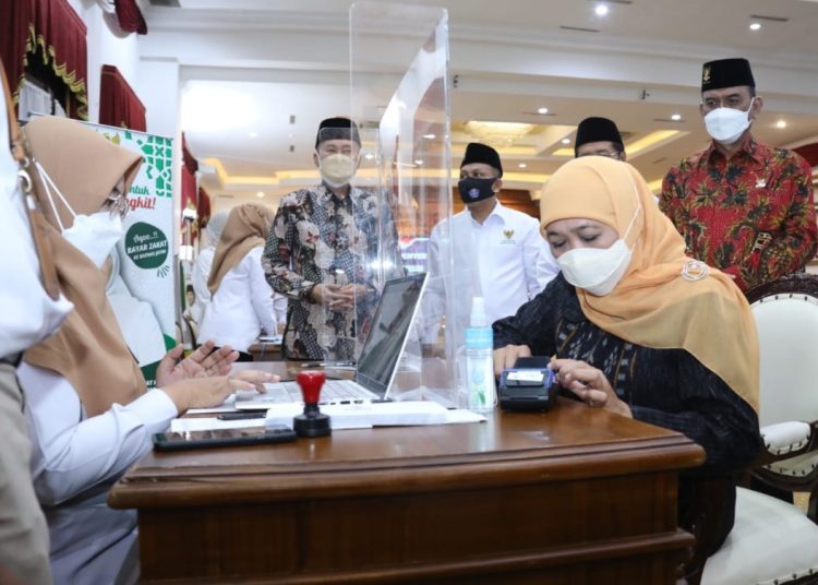 Gubernur Jatim Khofifah Indar Parawansa menyerahkan zakat melalui Baznas. Pembayaran zakat ini selain bisa dilakukan secara tunai, juga bisa dilakukan melalui pembayaran non tunai atau QRIS.