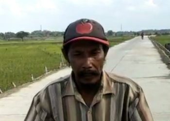 Seorang warga Desa Tanggungan Kecamatan Boureno dengan latar belakang jalan yang sudah dicor.