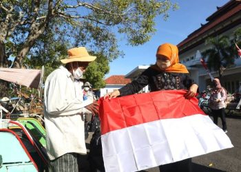 Gubernur Jawa Timur Khofifah Indar Parawansa membagikan bendera merah putih kepada salah satu tukang becak di halaman Kantor Bakorwil Kabupaten Pamekasan.