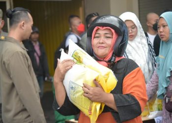 Seorang ibu membawa beras yang dibelinya dari operasi pasar di Pasar Tambahrejo.