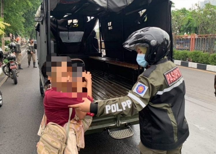 Personel Satpol PP Surabaya melakukan razia dan mengamankan ibu-anak mengemis di traffic light.